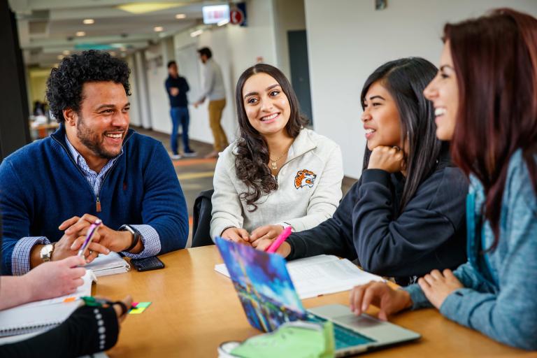 Students sitting at a table and talking in a hallway
