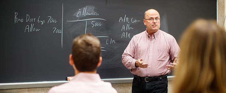 Professor speaks to students in front of a chalkboard.