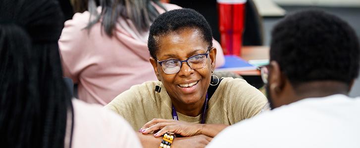 Smiling person with glasses and short hair engaging in a group discussion.