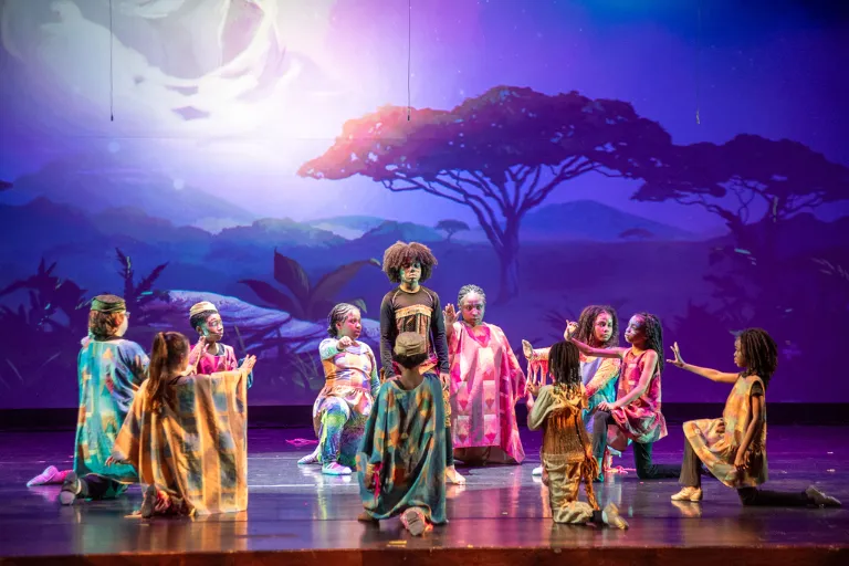 Colorful stage performance with children in African attire before a moonlit landscape.