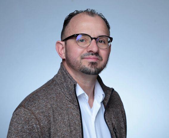 Man in glasses, with beard and mustache, in white shirt and grey jacket
