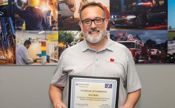 Photograph of a smiling man in grey shirt and glasses holding a framed certificate.