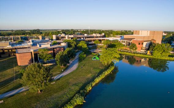 Aerial photograph of university buildings, a serene lake, and lush green landscape.