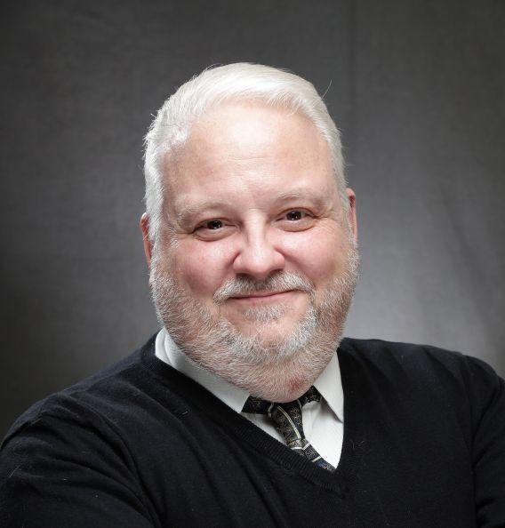 Man with beard, wearing dark sweater and tie with white button-down shirt