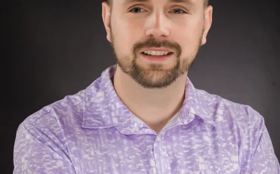 Professional headshot of man with short beard in purple and white short-sleeved shirt